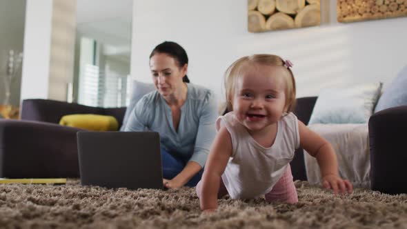 Caucasian mother using laptop while baby crawling on the floor at home