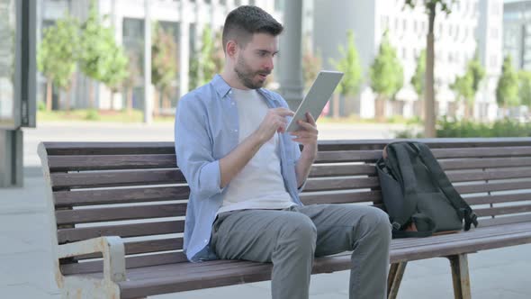 Young Man Celebrating Online Win on Tablet While Sitting on Bench