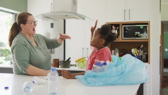 Happy caucasian woman and her african american daughter sorting waste together