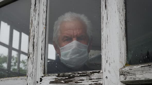 Man In Medical Mask Looks Sadly Out Of Window At Street Because Of The Pandemic