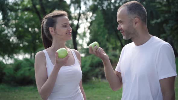 Happy Sportive Man and Woman Eating Green Apples After Training and Smiling at Camera. Portrait of