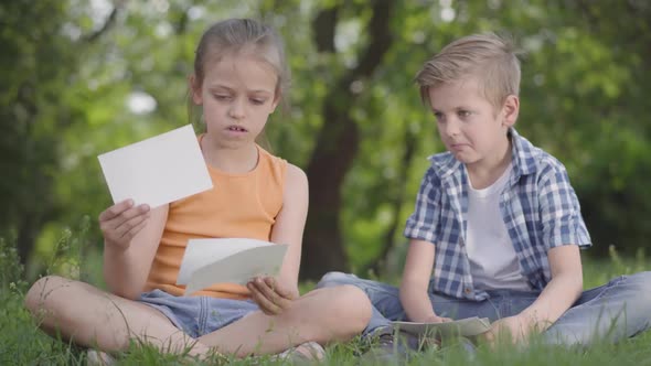 Portrait of Cute Handsome Boy in Checkered Shirt and Girl with Long Hair Looking at Sheets of Paper