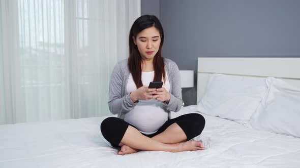 pregnant woman using smartphone on a bed