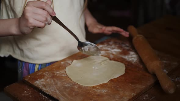 Child Sprinkles Flour on Dough so That Rolling Pin Does Not Stick to Flatbread