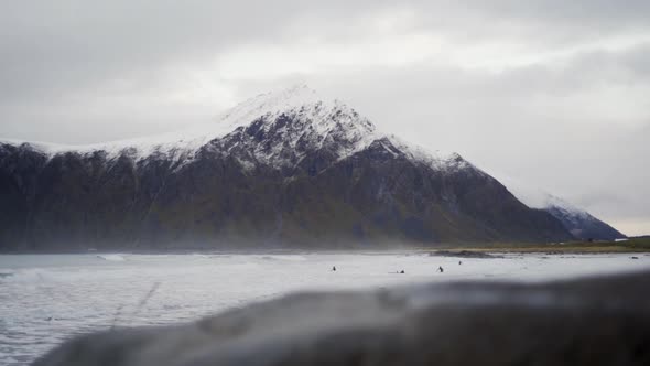 Surfers In Cold Sea Under Snow Capped Mountain