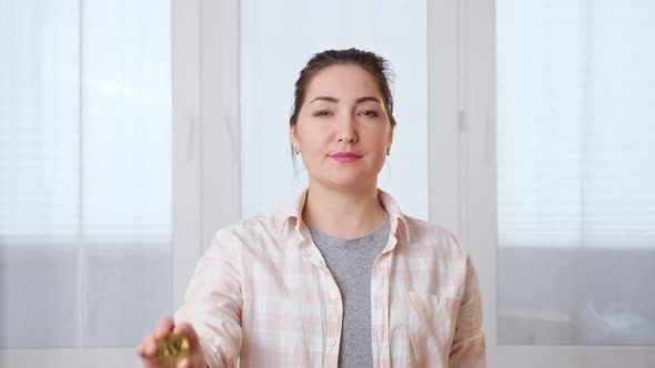 Young Woman Holding a Gold Coin of Cryptocurrency in Her Hand and Smiling Against the Background 