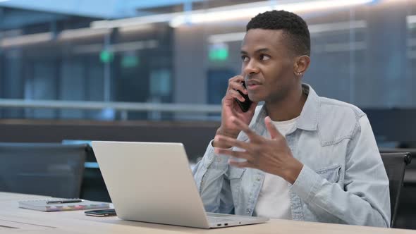 African Man with Laptop Talking on Smartphone