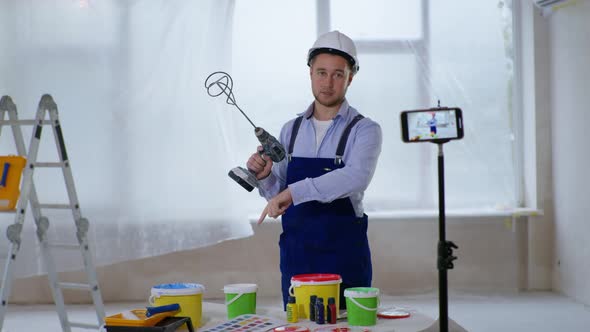 Male House Painter Records Video on Smartphone and Mixes Paint in Bucket for Painting Walls Indoors