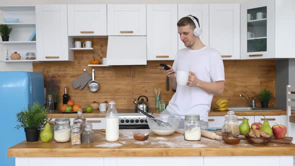 Young Man Using Mobile Phone In Kitchen At Home Wearing Headphones