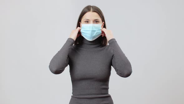 Caucasian Woman In Gray Turtle Neck Dress On A Grey Background Take A Face Mask Off