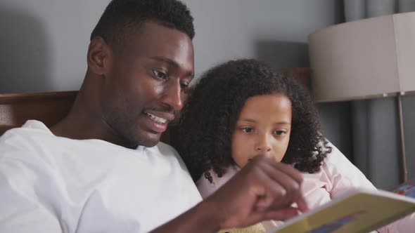 African american father reading a story to his daughter in bed