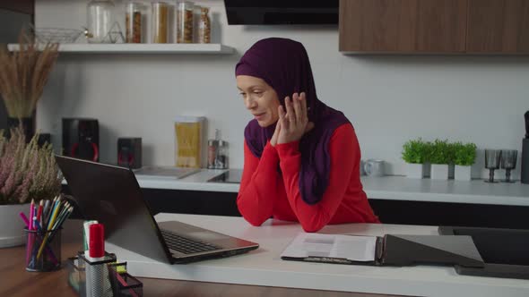 Cheerful Charming Arab Hijab Woman Making Video Call Online Using Laptop Pc Indoors