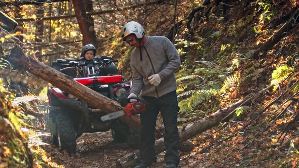 An Autumn Forest - Man Turns on a Chainsaw in the Woods and His Son Is Waiting for Him on a Quad