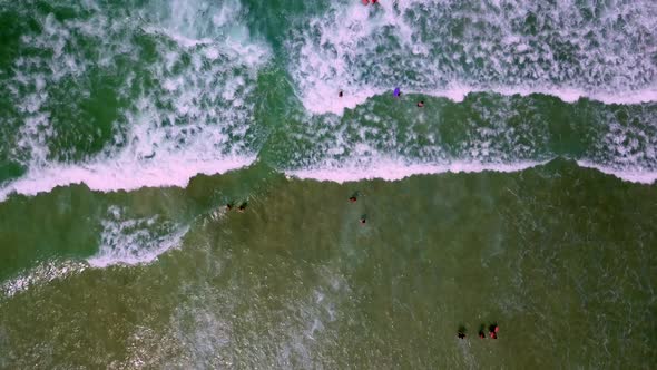 Aerial top down shot of people walking through the sea waves breaking on the beach