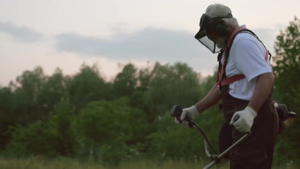 Male Worker in Overalls and Protective Mask Cutting Grass