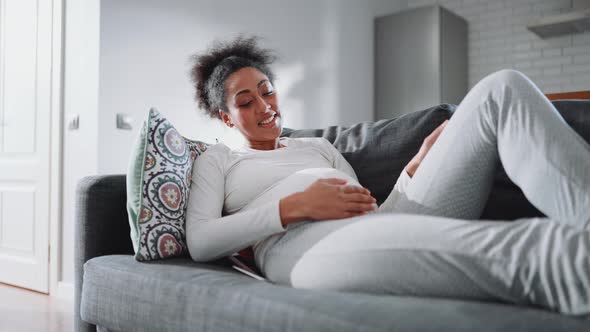 Positive African pregnant woman lying on the couch