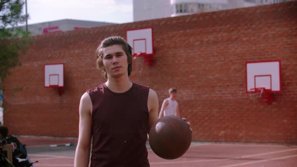 Young Man Standing on the Basketball Playground and Hitting the Ball