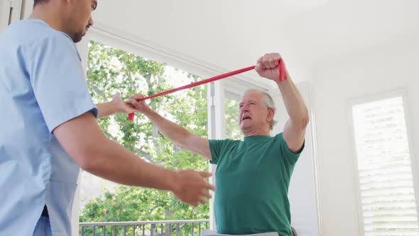 Male physiotherapist examining retired senior man exercising with resistance band at retirement home
