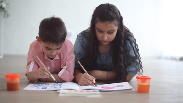 Happy Little Brother and Sister Paint with Paint in the Album Lying on the Floor and Smile