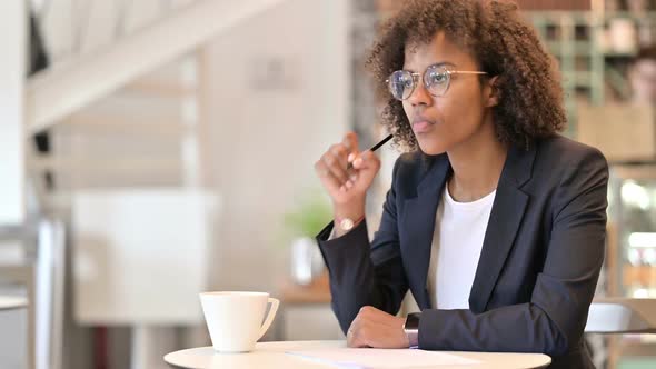 Pensive African Businesswoman Writing on Paper in Cafe