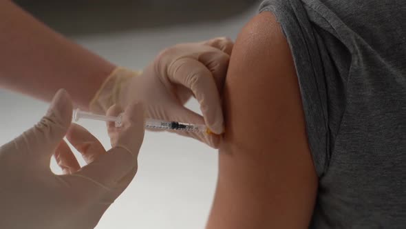 Closeup of Doctor in Medical Latex Gloves Giving Injection Vaccine Against Coronavirus During Mass