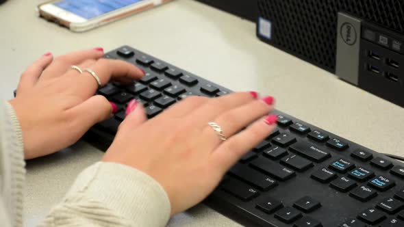 Close up of woman’s hands while typing on computer keyboard wearing a sweater