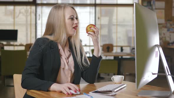Portrait of Pretty Young Woman Eating an Apple in Her Office