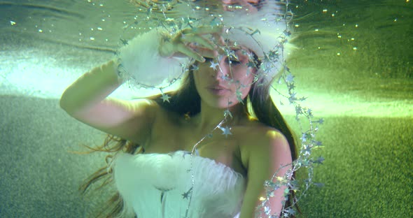 Brunette Woman Dressed in White Fur Hat and Gown Is Floating in Swimming Pool, Underwater Shot