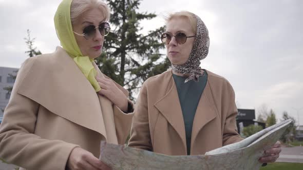 Close-up of Two Mature Women in Headscarves and Sunglasses Holding the Map and Talking