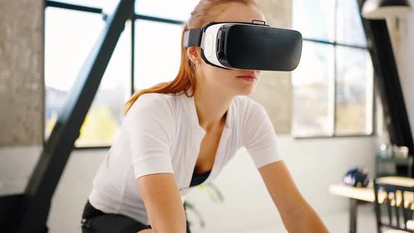 Young Lady in Sportswear and VR Glasses Pedaling Indoor Cycle Trainer