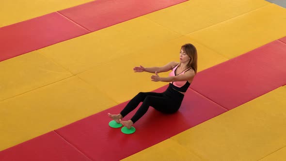 A beautiful, slender girl does exercises with sliding discs in the gym.