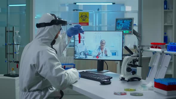 Lab Technician in Ppe Suit Holding Test Tube and Talking on Video Call with Doctor