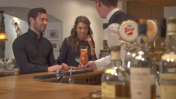 A man and woman couple having drinks at a bar in a restaurant.