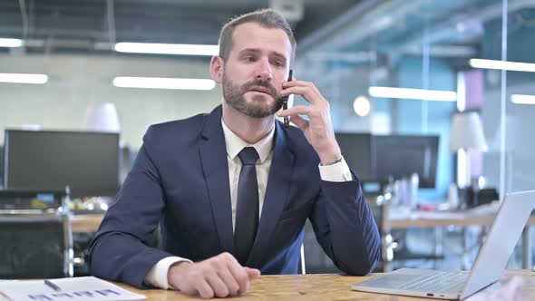 Cheerful Businessman Talking on Smartphone in Office