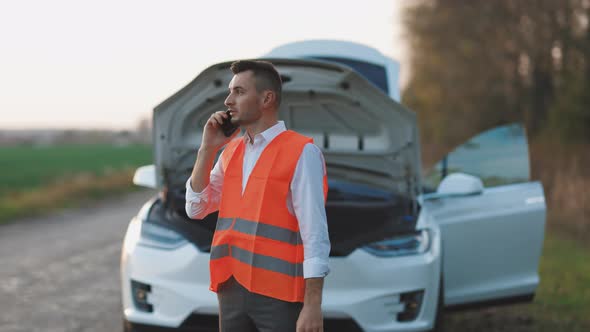 Man Calling Car Assistance Services Because His Electric Car is Broken