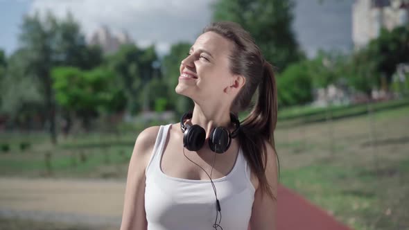 Joyful Caucasian Sportswoman Putting on Headphones and Leaving. Portrait of Happy Beautiful Woman