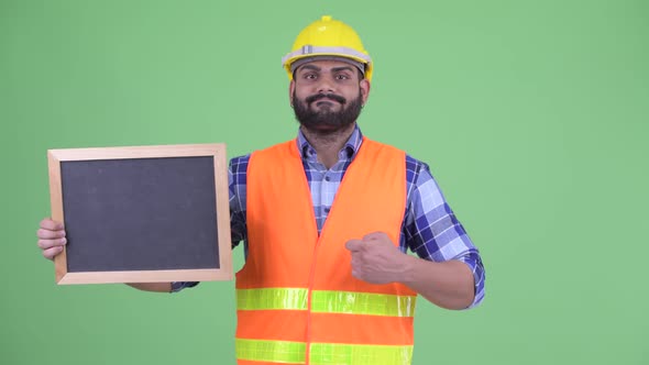 Stressed Overweight Bearded Indian Man Construction Worker Holding Blackboard and Giving Thumbs Down