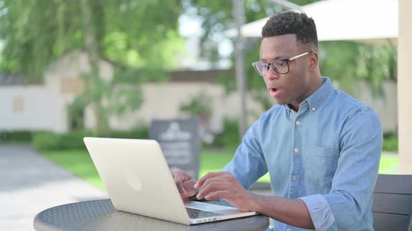 Successful African Man Celebrating on Laptop in Outdoor Cafe