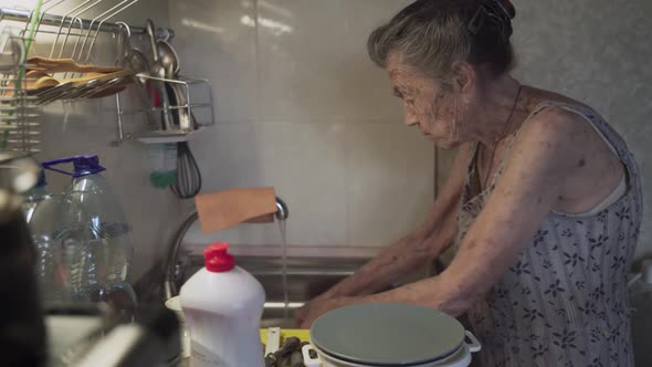Lonely Sad Senior Woman 90 Years Old with Gray Hair Forced to Wash Dishes with Her Hands Due to