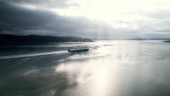 The brilliant morning sun streams through dark gloomy clouds as a ferry passes, Aerial orbit
