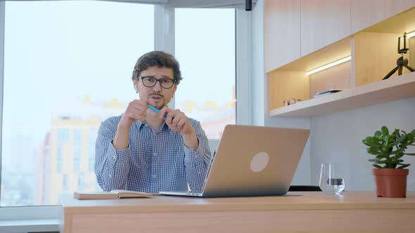 Young man sits in front of a laptop, looks into the camera and communicates with the audience.