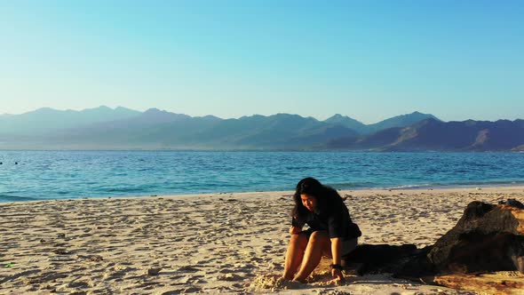 Beautiful smiling girl on photoshoot by the sea at the beach on summer white sand and blue backgroun