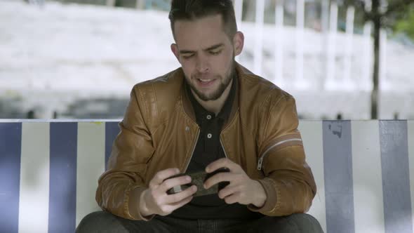 Smiling Young Man Looking at Smartphone Outdoor