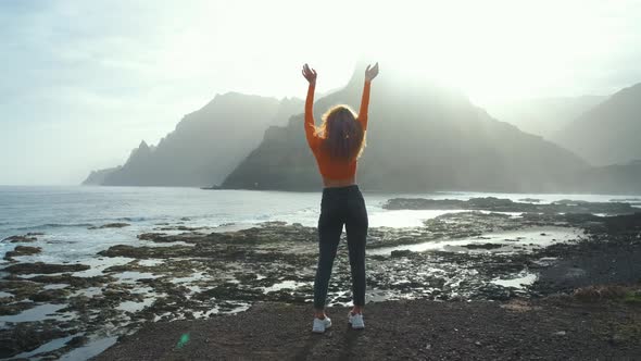 A Woman Walks Next to the Ocean and Raises Her Hands Up and Enjoying the Moment on Volcanic Beach of