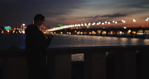 Man Using Smartphone Walking in a City Embankment at Twilight