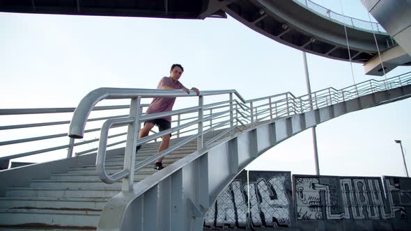 a Freerunner Jumping Off a High Ladder Onto Gravel Against the Background of Graffiti Under a Bridge
