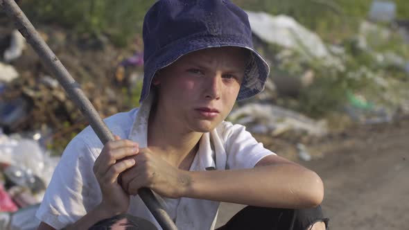 Dirty Faced Boy Crouching at Landfill