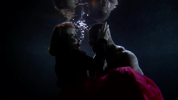 An African-American Man and a Blonde Female Girl, They Are at the Depth of the Water on a Dark