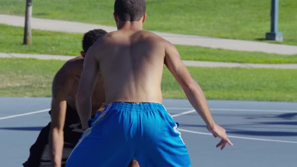 Friends playing basketball at park, one on one