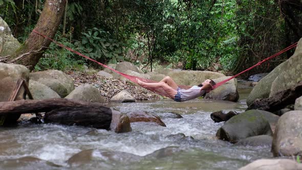 A young asian woman lying and relaxing in hammock in waterfall stream